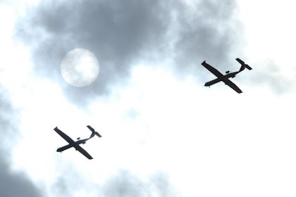 Two planes follow each other through the clouds and in front of the moon.
